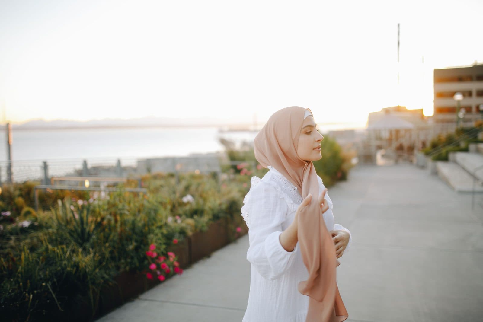 Mulher de lenço champanhe e vestido branco caminha serena ao pôr do sol