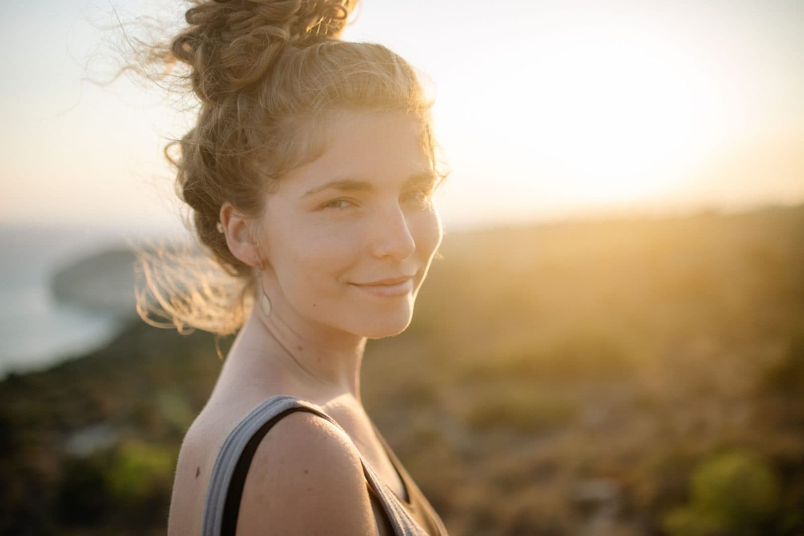 Jovem sorri tranquila ao ar livre, iluminada pela luz dourada do fim de tarde