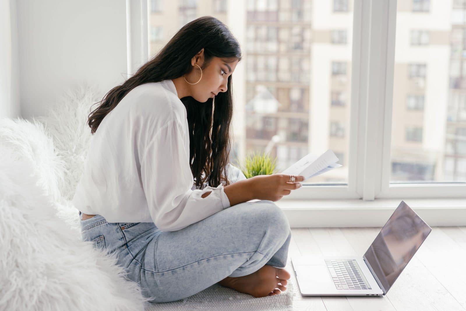 Mulher lê documentos com serenidade sentada ao lado de janela ampla