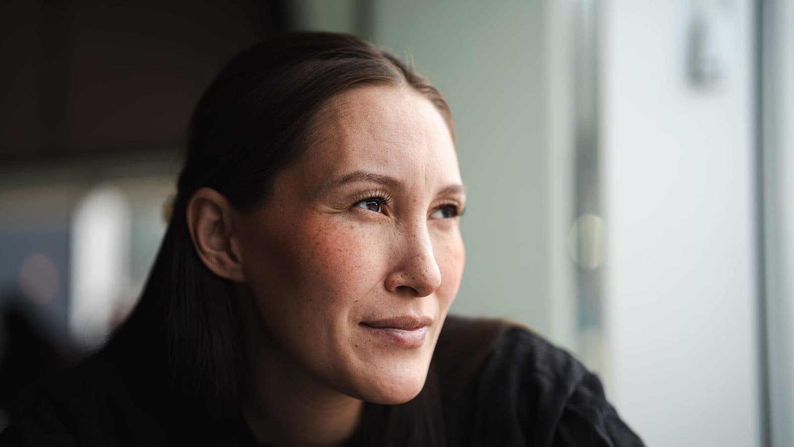Mulher serena olha pela janela em retrato próximo com luz natural suave