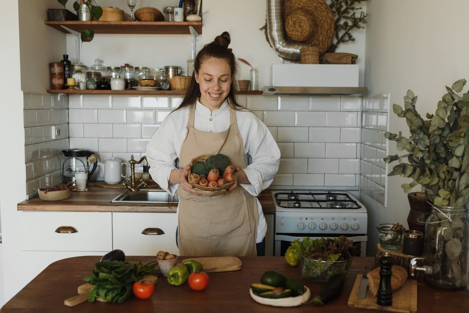 Mulher de avental segura cesta de legumes frescos em cozinha acolhedora