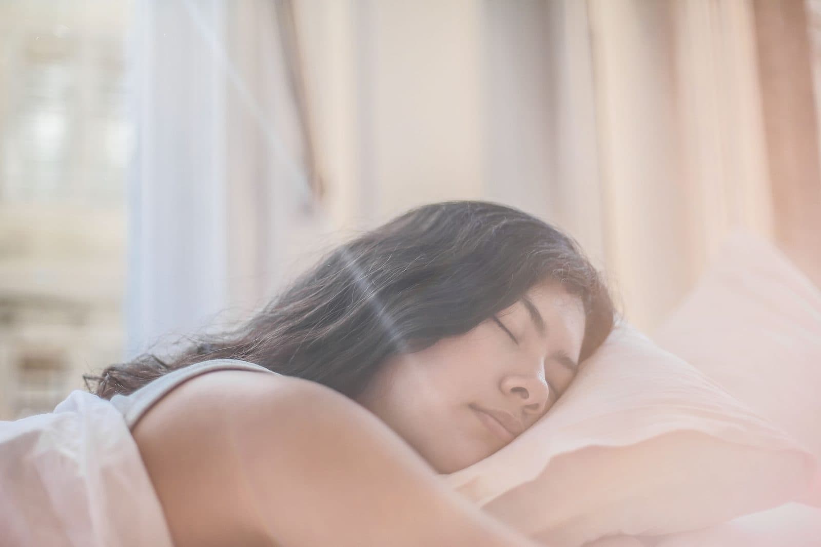Mulher dorme tranquila em travesseiro claro sob luz suave cor de pêssego